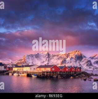 Schönen Fischerdorf mit Boote bei Sonnenaufgang, Lofoten, Norwegen. Die winterliche Landschaft mit Häusern, schneebedeckte Berge, Meer, Boote, farbenfrohen Himmel mit Stockfoto