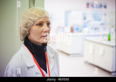 Mitarbeiter der Bierherstellung Labor. Junge Lab Assistant, in ein weißes Gewand gekleidet, steht auf Bier Lagerverwaltung. Vor dem Hintergrund der hellen Zimmer chemisches Labor, einem Arbeitsbereich Stockfoto