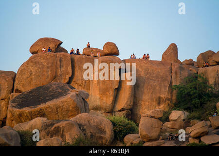 Westliche Touristen und Back Packers knüpfen und einen Sonnenuntergang auf einem großen Boulder und Red Rock Formation in Hampi, Indien genießen. Stockfoto
