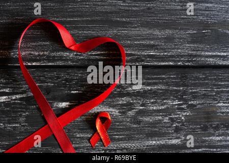 Closeup red ribbon in Form von Herzen Bewußtsein auf schwarzen Holztisch Hintergrund für den Welt-AIDS-Tag Kampagne. Stockfoto