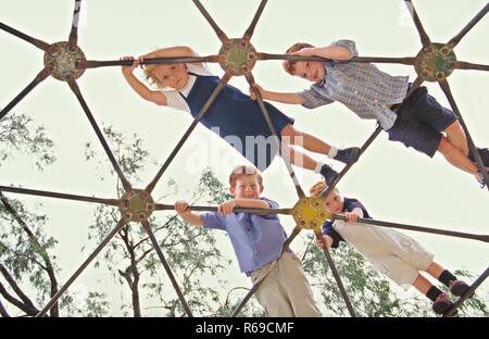 Porträt, Froschperspektive, 4 rothaarige Kinder, 3-6 Jahre, Klettern ueber ein kuppelfoermiges Klettergeruest auf einem Spielplatz Stockfoto