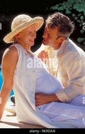 Outdoor, Profil, blonder Mann moechte seine schwangere weiss gekleidete Frau mit Strohhut kuessen Stockfoto