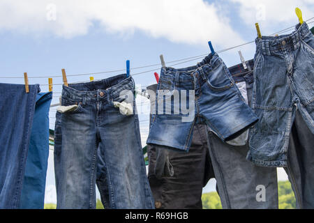 Jeans in verschiedenen Farben und Größen hängen an einer Wäscheleine zum Trocknen Stockfoto