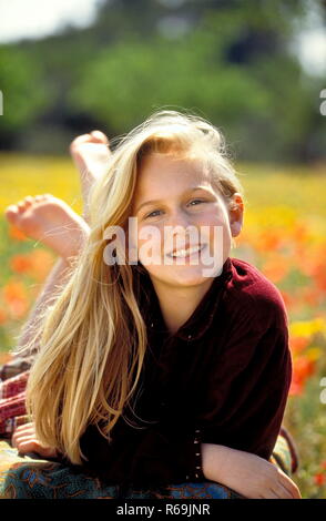 Porträt, laechelndes blondn Maedchen mit langen Haaren, 13 Jahre, bekleidet mit weinroter Samtjacke, Balatonfüred barfuss auf einer mit Klatschmohn und gelben Blueten uebersaeten Wiese Stockfoto