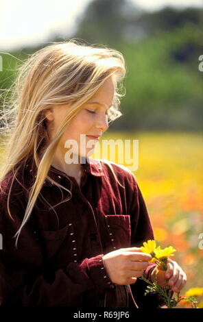 Porträt, laechelndes blondn Maedchen mit langen Haaren, 13 Jahre, bekleidet mit weinroter Samtjacke, Balatonfüred barfuss auf einer mit Klatschmohn und gelben Blueten uebersaeten Wiese Stockfoto