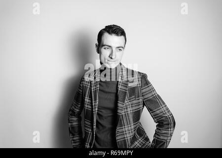 Close up Schwarz-Weiß-Porträt einer jungen Mann mit Rollkragen Pullover und Jacke, an der Seite, gegen normales studio Hintergrund Stockfoto