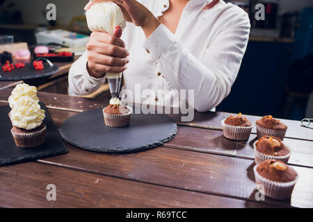 Frau, Frischkäse top auf Cupcakes in der Küche. Kochen Kuchen. Stockfoto