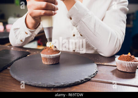 Frau, Frischkäse top auf Cupcakes in der Küche. Kochen Kuchen. Stockfoto