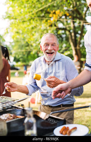 Ein älterer Mann stand vom Grill, holding Mais auf einer Grillparty. Stockfoto