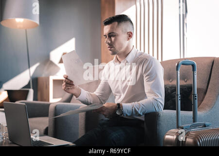 Junge Unternehmer sitzen in der Lobby des Hotels mit seinem Gepäck Stockfoto