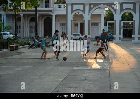 Kubanischen Jungen Fußball spielen auf dem Hauptplatz von Cienfuegos, Kuba als die Sonne beginnt zu setzen Casting ein goldenes Leuchten auf der Straße Stockfoto
