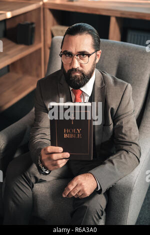 Dunkelhaarige bärtigen Mann hält die Heilige Bibel Stockfoto