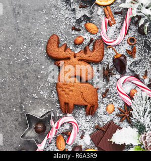 Weihnachten Lebkuchen elk Form Cookie mit Cutter, Candy Cane und Gewürzen auf grauem Beton Tabelle mit Schnee. Urlaub Backen oder kochen Zutaten. Ch Stockfoto