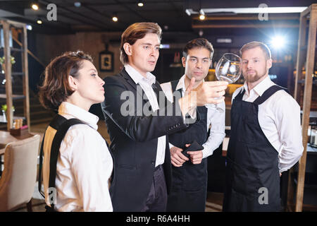Professionelle männliche Manager im schwarzen Anzug arbeiten mit Kellner in der modernen Einrichtung: Er zeigt, wie die Sauberkeit der Wineglass zu überprüfen, um zu staf Stockfoto