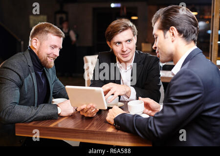 Positive selbstbewussten jungen Geschäftspartner in formalen Jacken am kleinen Tisch sitzen im Restaurant und Diskutieren über Kaffee Stockfoto