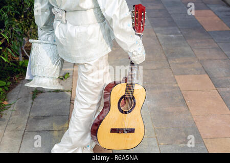 Street artist in weiss silber Lack wandern im City Park gemalt. Lebende statue Interpret mit Gitarre Stockfoto