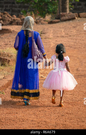 Eine indische Frau in einem bunten Saris geht Hand in Hand mit ihrer Tochter tragen ihre beste rosa Kleid bei einem Familienausflug. Stockfoto