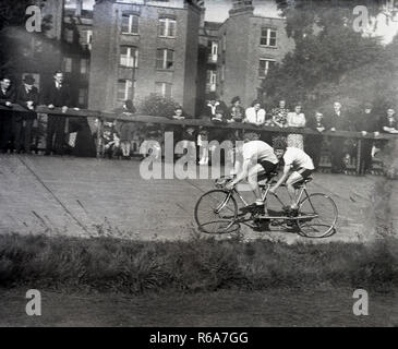 1940 s, historischen, zwei rennradfahrer auf einem Tandem Radfahren außerhalb in einem Radrennen auf ein Bankkonto konkrete Spur, von den Zuschauern hinter einem Zaun, England, UK stehen sah. Stockfoto