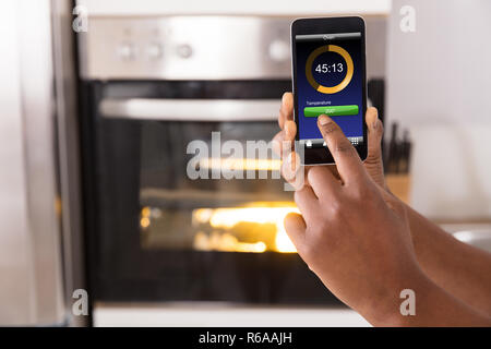 Frau Betriebssystem Backofen Appliance mit Handy App Stockfoto