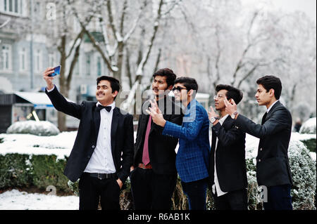 Gruppe von 5 indische Studenten in Anzügen stellten im Winter im freien Tag und selfie am Telefon. Stockfoto