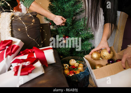 Paar Vorbereitung Wohnzimmer für Weihnachten abend Feiern, Dekorieren Baum mit Glocken, goldenen Kugeln, Lichterketten und Geschenke und Geschenk Stockfoto