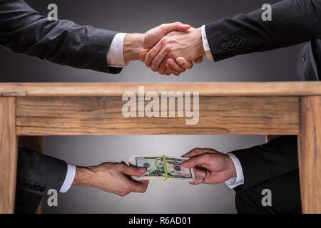 Geschäftsleute, die Hände zu schütteln und die Bestechung unter dem Tisch Stockfoto