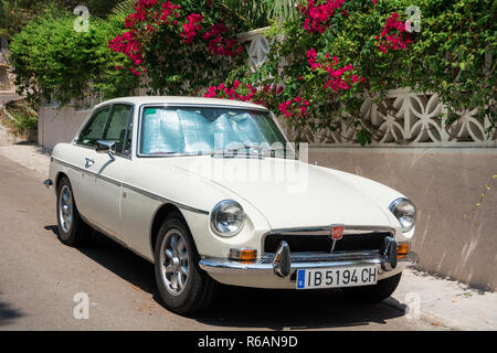 Santa Ponsa, Mallorca, Spanien - 24. Juli 2013: Retro Car MG BGT ist in der Nähe einer Wand mit Blumen und Palmen Blätter geparkt. Stockfoto