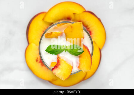 Pfirsich Joghurt mit Minze in ein Glas mit frischem Obst auf weißem Marmortisch. gesundes Frühstück. top View Stockfoto