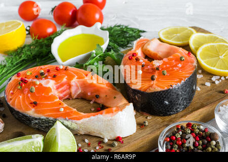 Roher Lachs Steaks mit Gewürzen, Kräutern, Tomaten und Zitronen auf Holz Schneidebrett über weiß Holz- Hintergrund. Gesunde Ernährung Lebensmittel. Nach oben Schließen Stockfoto