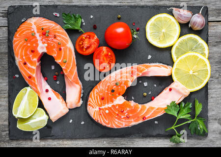 Roher Lachs Steaks mit Gewürzen, Kräutern, Tomaten und Zitronen auf schwarzem Schiefer. Gesunde Ernährung Lebensmittel. Kochen Konzept. top View Stockfoto