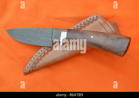 Ein Damaskus skinner Messer und Scheide sind oben auf einem hellen orange Hintergrund Stoff angezeigt. Stockfoto