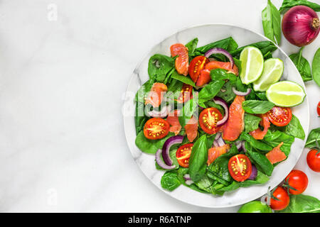 Frischer Salat mit Lachs, Spinat, Tomaten, roten Zwiebeln und Basilikum in Marmor Platte auf weißem Marmortisch. gesunde Ernährung Konzept. Ansicht von oben mit der Kopie Stockfoto
