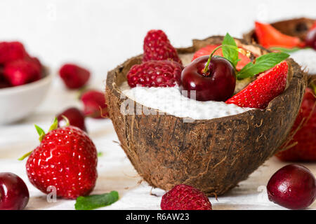Chia Milchreis mit frischen Erdbeeren, Himbeeren, Kirsche und Minze in Kokosnuss Schale mit Löffel. gesundes Frühstück. Nach oben Schließen Stockfoto