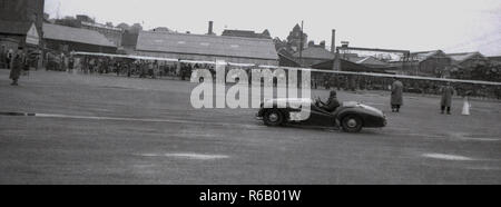 1950, historische, an einem Industriestandort, eine ungewöhnliche offenen Sportwagen entlang gefahren wird, von den Zuschauern beobachtet. Stockfoto