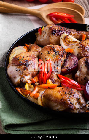 Gebratene Chile miso Chicken Drumsticks mit Gemüse in Gusseisen Skillet auf rustikalen Holztisch, Nahaufnahme, selektiven Fokus Stockfoto