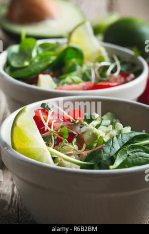 Frisches Gemüse Salat mit Avocado und Quinoa, Spinat, Gurken, Tomaten, grüne Zwiebeln und Kalk auf rustikalen Holztisch Stockfoto