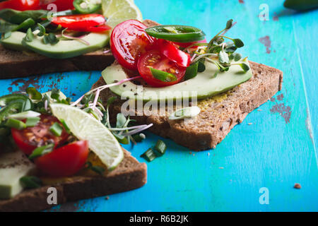 Mexikanische avocado Toasts mit Gemüse, frischen Spinat, Tomaten, grüne Zwiebeln, Chili, Sprossen und Kalk auf rustikalen Tisch Stockfoto