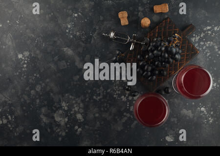 Rotwein in Glas Becher mit Trauben auf einem dekorativen Board. Auf einem dunklen Hintergrund. Ansicht von oben mit Platz für Text. Stockfoto