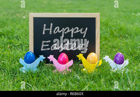 Eastercard mit schiefertafel und bunte Ostereier in Eierbecher auf einer Wiese Stockfoto