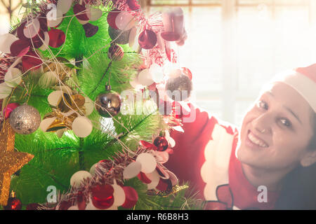 Schöne junge Frau in Santa Hut schmücken Weihnachtsbaum zu Hause Stockfoto