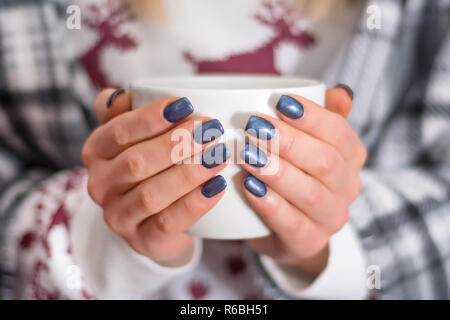 Weibliche Hände mit navy blue Maniküre color Holding Tasse Tee. Winter Maniküre Farbkonzept. Close Up, selektiver Fokus Stockfoto