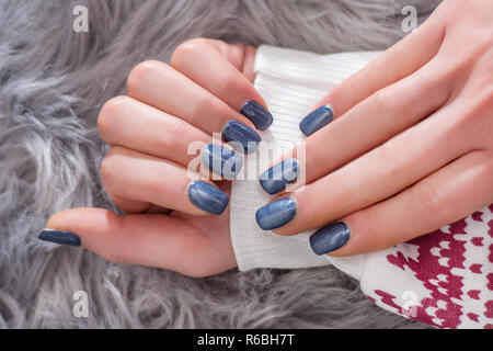 Mädchen Hände mit navy blue Nagellack Farbe auf Winter Pullover und Grau haarige Hintergrund. Maniküre Konzept Bild. Close Up, selektiver Fokus Stockfoto