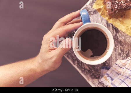 Chocolate Brownie bestreut mit Kakao und Kokosnuss im Hintergrund mit Hand der Männer nimmt eine kaffeetasse an der Ecke einen Tisch in der Nähe eines Fensters. Lager Stockfoto