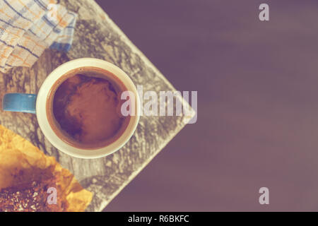 Chocolate Brownie bestreut mit Kakao und Kokosnuss im Hintergrund mit einem kaffeebecher an der Ecke einen Tisch in der Nähe eines Fensters. Matt Effekt. Stock pho Stockfoto