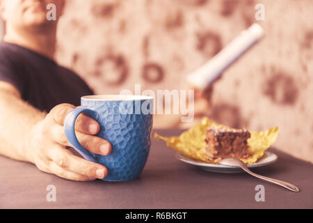 Junger Mann Lesen einer Zeitschrift in einem Cafe. In der einen Hand eine Tasse Kaffee, in der anderen eine Zeitung. Blick aus dem Fenster hinter ihm. Foto Stockfoto