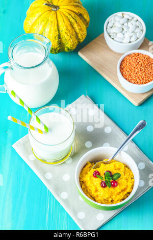 Kürbis Brei. Leckere hausgemachte Kürbis Porridge mit Cranberry und Minze in einem weißen grüne Platte auf dem Tisch, bereit, mit Milch zu essen. Blau turquo Stockfoto