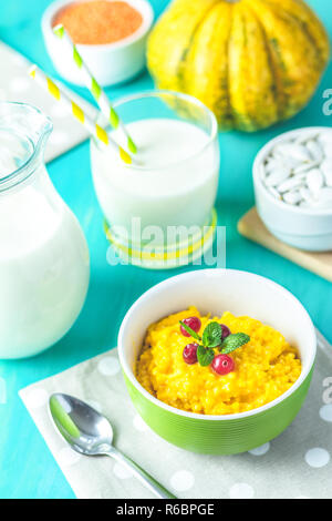 Kürbis Brei. Leckere hausgemachte Kürbis Porridge mit Cranberry und Minze in einem weißen grüne Platte auf dem Tisch, bereit, mit Milch zu essen. Blau turquo Stockfoto