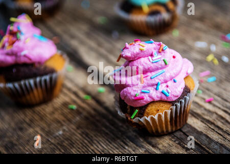 Chocolate Cupcake mit farbigen Rosa und grün Creme auf Holz Tisch Stockfoto