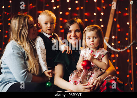 Zwei Mütter sitzen mit niedlichen Kinder Weihnachtsgeschenke. Stockfoto