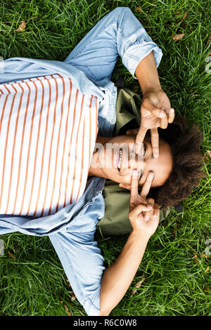 Blick von oben auf einen fröhlichen jungen Jugendjungen Festlegung auf ein Gras, Frieden Geste Stockfoto